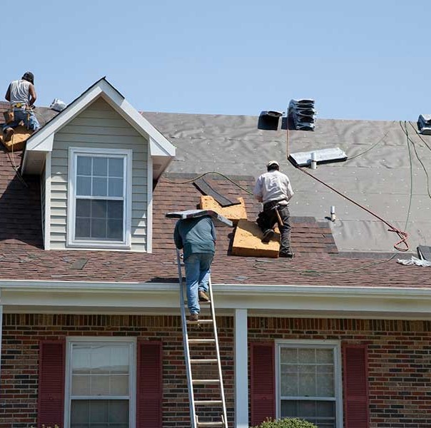 Close up of workers on a residential roof installing brand new red-ish asphalt shingles